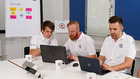 Drei Männer sitzen an einem Tisch im Konferenzraum vor ihren Laptops.